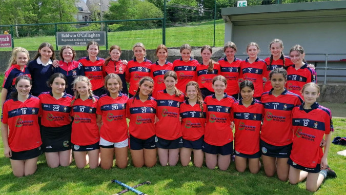 Eine Gruppe von jungen Athletinnen in rot-schwarzen Uniformen auf einem Rasenfeld auf dem Gelände der St. Mary's Secondary School in Macroom.