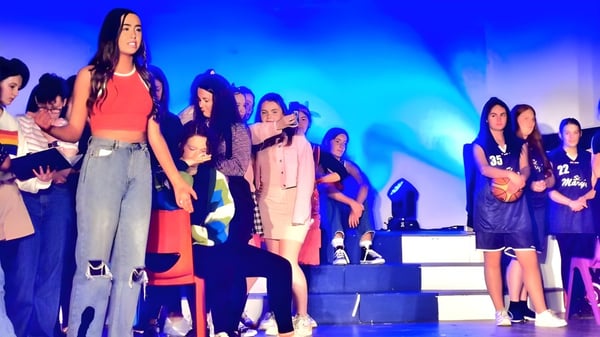 Eine Gruppe Schülerinnen der St. Mary’s Secondary School Baldoyle steht auf einer Bühne mit bunter Beleuchtung.