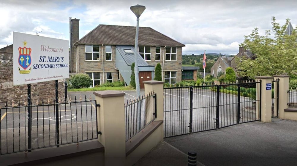 Das zweistöckige Backsteingebäude der St. Mary's Secondary School in Macroom mit markantem Dach und Metallzaun in einer Wohngegend.