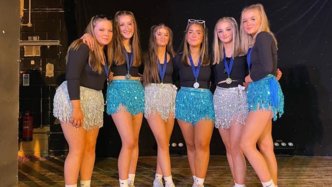 Eine Gruppe Schülerinnen der St. Mary's Secondary School Macroom posiert in bunten Kostümen auf einer Bühne.