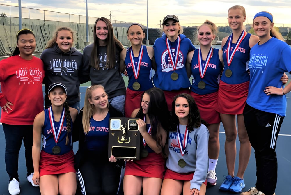 Eine Gruppe junger sportlicher Schülerinnen des St Mary’s District & Vocational Collegiate Institute posiert mit Medaillen auf einem Tennisplatz.