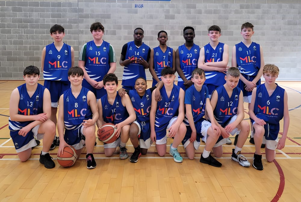 Eine Gruppe junger Basketballspielerinnen und Basketballspieler posiert in der Turnhalle des St. Mel’s College vor einer Backsteinwand.