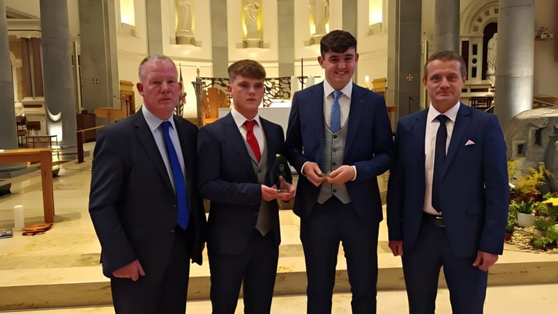 Vier Männer in formellen Anzügen stehen im Innenraum des St. Mel’s College zusammen.