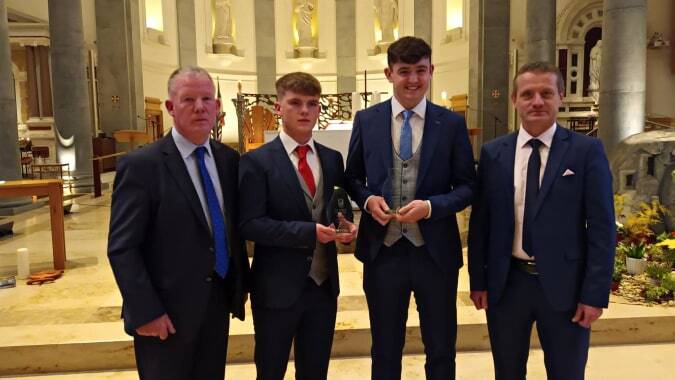 Vier Männer in formeller Kleidung stehen in einem reich verzierten Innenraum des St. Mel’s College.