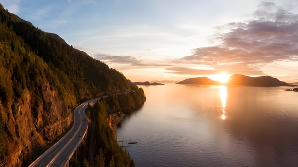 Eine Küstenstraße verläuft an steilen Klippen entlang mit Blick auf ruhiges Wasser bei Sonnenuntergang nahe der St. Michaels University School.