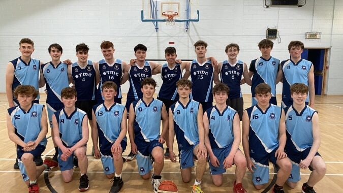 Die Basketballmannschaft des St. Michael's College posiert gemeinsam in der Sporthalle vor einem Basketballkorb.