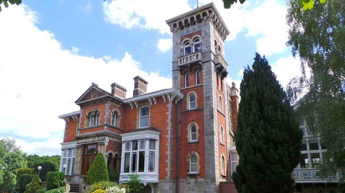 Das historische Backsteingebäude mit hohem Turm auf dem Campus von St. Michael's College umgeben von grüner Vegetation und blauem Himmel.