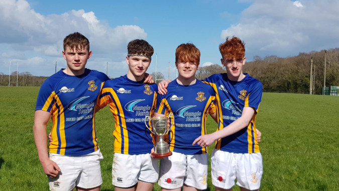Vier Schüler von St. Michael's College halten auf dem Sportfeld eine Trophäe bei bewölktem Himmel.