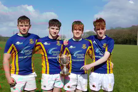 Vier Schüler des St. Michael's College in Sportuniformen halten gemeinsam einen Pokal auf einem Feld.
