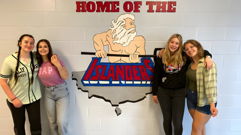 Vier Schülerinnen stehen vor dem großen Schild mit dem Schriftzug Home of the Islanders auf dem Gelände der St. Michael's Regional High.