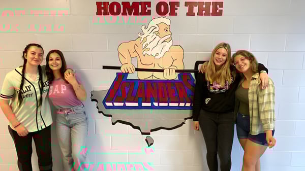 Vier Schülerinnen stehen vor dem großen Schild mit dem Schriftzug Home of the Islanders auf dem Gelände der St. Michael's Regional High.