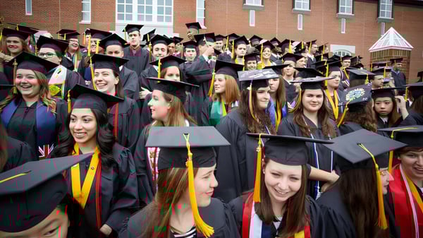 Eine große Gruppe von Absolventen in akademischer Kleidung feiert vor dem Backsteingebäude auf dem Campus der St. Michaels University School.