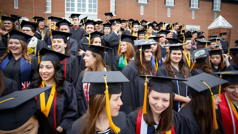 Eine große Gruppe von Absolventen in akademischer Kleidung feiert vor dem Backsteingebäude auf dem Campus der St. Michaels University School.