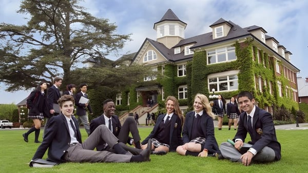 Schüler der St. Michaels University School sitzen in Schuluniform auf der Wiese vor dem mit Efeu bedeckten Hauptgebäude.