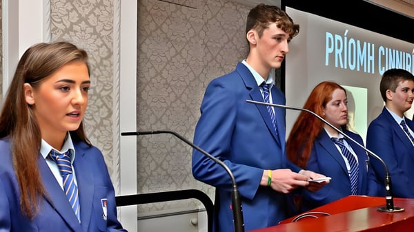 Eine Gruppe Schülerinnen und Schüler der St. Mogues College steht vor einem Hintergrund mit dem Schriftzug Priory Church.