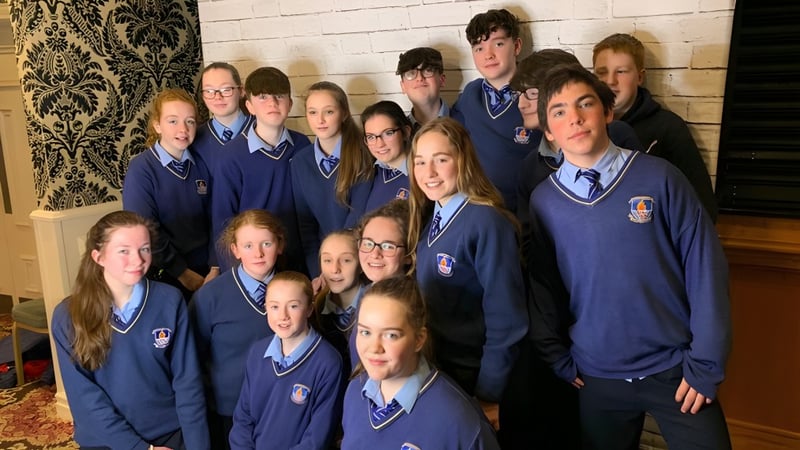 Eine Gruppe von Schülern in blauen Schuluniformen posiert vor einer gemusterten Wand auf dem Gelände des St. Mogues College.