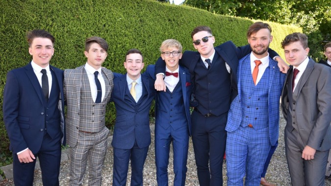 Eine Gruppe gut gekleideter Personen posiert bei einer formellen Veranstaltung vor einer grünen Hecke auf dem Campus des St. Patrick's College.