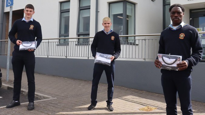 Drei Schülerinnen und Schüler des St. Patrick's College stehen vor einem Gebäude mit Glasfenstern und Metallgeländer.