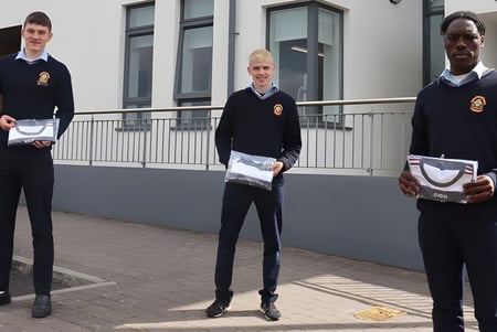 Drei Schülerinnen und Schüler des St. Patrick's College stehen vor einem grauen Gebäude mit Fenstern.