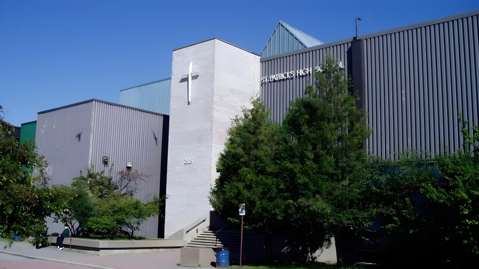 Das moderne mehrstöckige Gebäude von St. Patrick's High School ist von grüner Vegetation umgeben unter klarem blauem Himmel.
