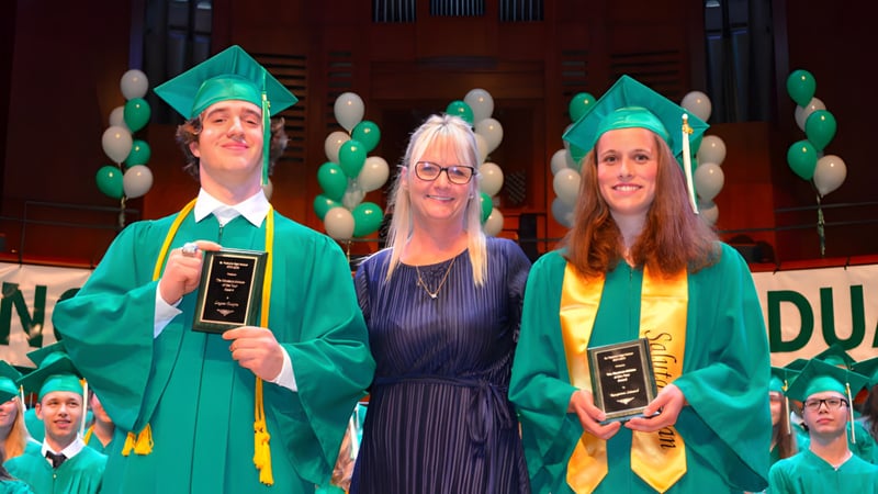 Drei Schüler der St. Patrick’s High School in Québec City in Abschlusskleidung mit Diplom vor grün-gelber Ballonwand.
