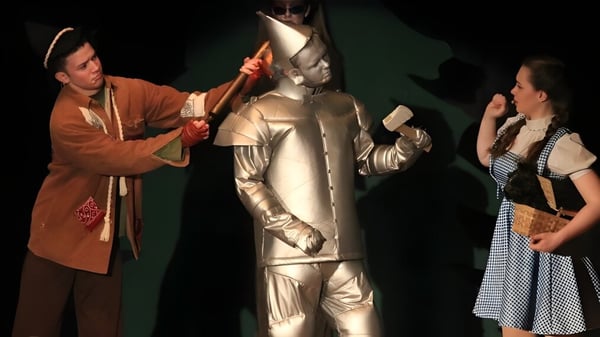 Drei Schülerinnen und Schüler von St. Patrick's High School in Theaterkostümen auf einer dunklen Bühne.