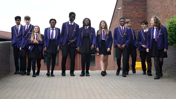 Eine Gruppe Schüler in Schuluniformen steht vor einem Backsteingebäude auf dem Gelände der St. Paul Catholic High School.