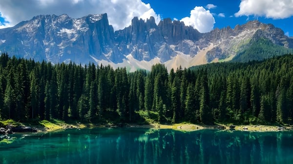Ein türkisfarbener Bergsee mit schneebedeckten Gipfeln und immergrünem Wald im Vordergrund.