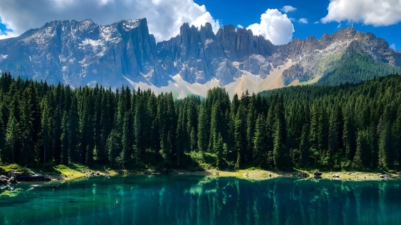 Ein türkisfarbener Bergsee mit schneebedeckten Gipfeln und immergrünem Wald im Vordergrund.