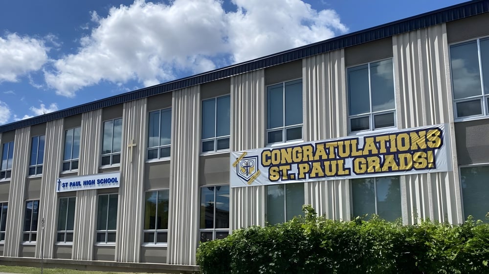 Das Gebäude der St. Paul High School mit einem Banner, das den Absolventen gratuliert, vor blauem Himmel mit Wolken.
