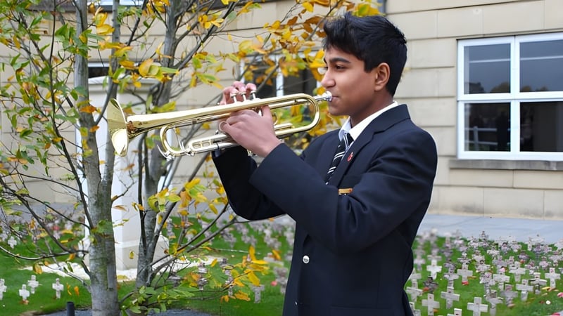Ein Schüler der St. Paul’s School spielt ein Blechblasinstrument vor herbstlicher Kulisse und einem Schulgebäude.