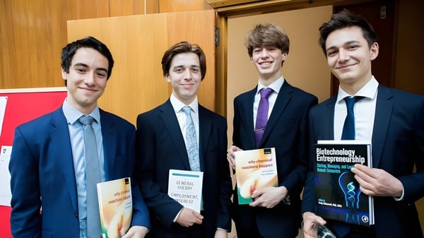 Vier Schülerinnen und Schüler der St. Paul’s School stehen in geschäftlicher Umgebung mit Büchern und Dokumenten.