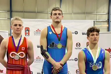 Drei Sportler mit Medaillen stehen vor einem Banner auf dem Gelände der St. Peter Catholic High School.