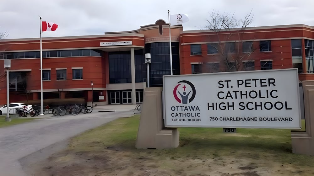 Das Backsteingebäude der St. Peter Catholic High School mit kanadischer Flagge und abgestellten Fahrrädern davor.
