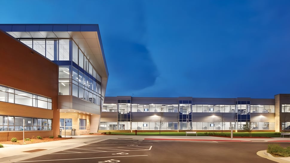Das moderne mehrstöckige Gebäude der St. Peter High School mit großen Glasfenstern und orangefarbener Fassade steht unter klarem blauem Himmel.