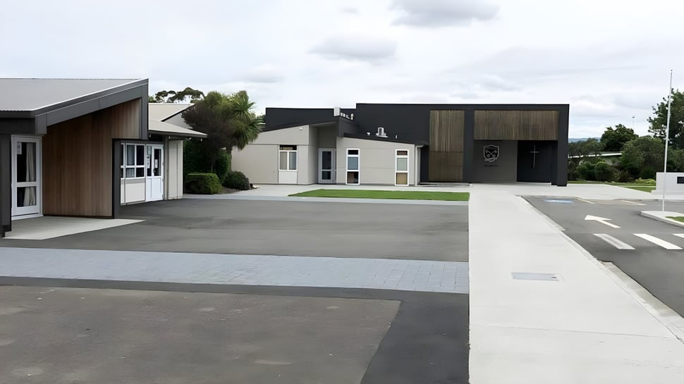 Das moderne Gebäude von St. Peter's College mit gepflasterter Einfahrt und angelegten Grünflächen unter bewölktem Himmel.