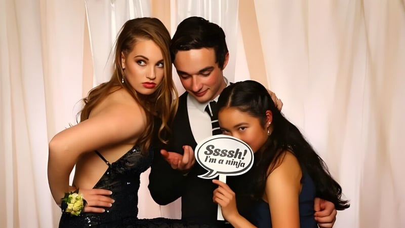 Drei Personen posieren beim Fotoevent am St. Peter's College, wobei die Frau in der Mitte ein Schild mit der Aufschrift 'Sssh! I'm a ninja' hält.