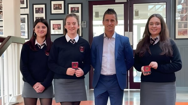 Vier Personen in formeller Kleidung stehen im Flur der St. Peter's Community School neben dekorativen Bildern an der Wand.