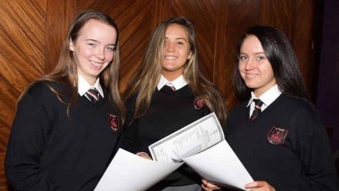 Drei Schüler der St. Peter's Community School tragen Schuluniformen und halten Papiere in einem holzvertäfelten Raum.