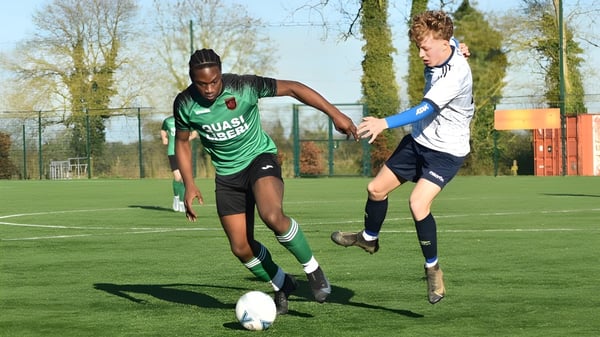 Zwei Schüler der St. Peter's Community School spielen Fußball auf einem Spielfeld mit Bäumen und Gebäuden im Hintergrund.