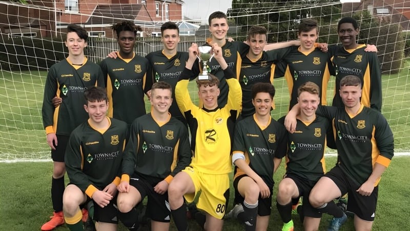 Eine Gruppe Schüler der St. Peter’s High School posiert mit einer Fußballtrophäe auf dem Spielfeld vor einem Backsteingebäude.