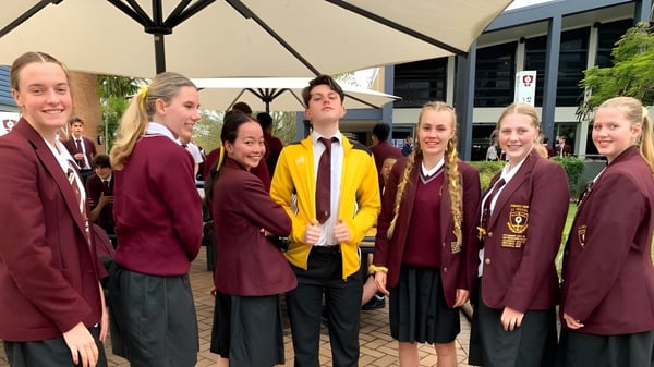 Eine Gruppe von Schülern des St. Peters Lutheran College steht im Freien zusammen unter einem Sonnenschirm.