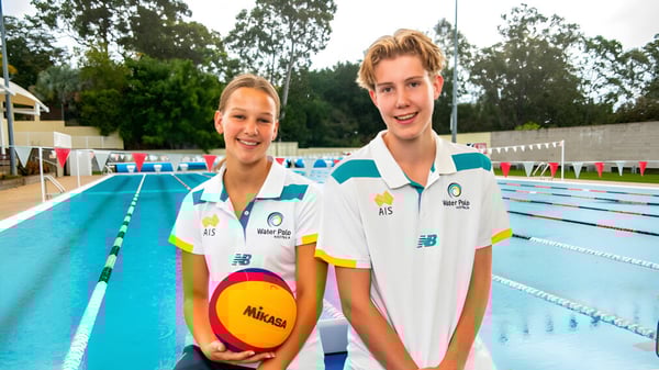 Zwei junge Athleten in Sportkleidung neben dem Schwimmbecken auf dem Campus von St. Peters Lutheran College halten einen Volleyball.