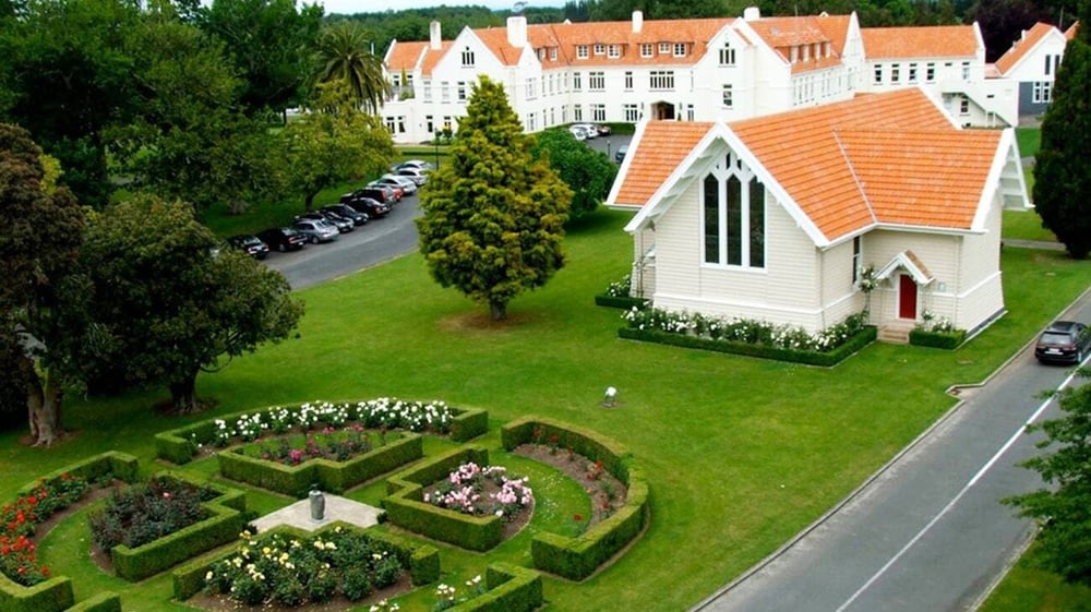 Das Schlossähnliche Hauptgebäude der St. Peter's School Cambridge umgeben von gepflegten Gärten und einem Weg im Vordergrund.