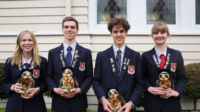 Vier Schüler in Schuluniform stehen vor einem Holzgebäude auf dem Gelände der St. Peter's School Cambridge und halten jeweils einen kleinen Hund.