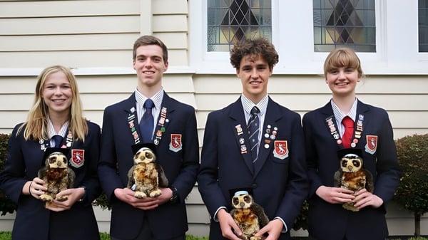 Vier Schülerinnen und Schüler der St. Peter's School Cambridge stehen vor einem Holzgebäude und halten jeweils einen kleinen Hund.
