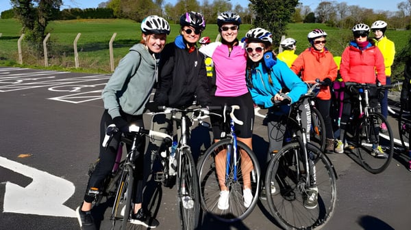 Eine Gruppe von Schülerinnen und Schülern der St. Raphaela’s Secondary School in bunter Radbekleidung posiert auf einer Straße vor einer grünen Wiese.