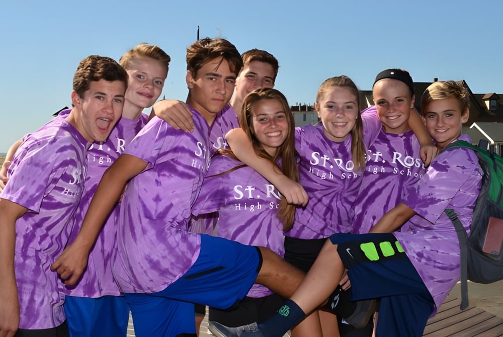 Eine Gruppe von Schülerinnen und Schülern der St. Rose High School trägt lila Batik-T-Shirts und steht gemeinsam auf einem Holzdeck.