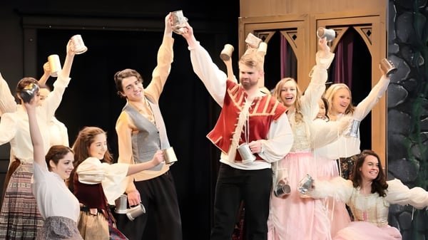 Schüler der St. Rose High School führen in bunten Kostümen eine Bühnenaufführung vor dunklem Hintergrund auf.