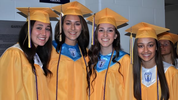 Eine Gruppe Schülerinnen der St. Rose High School steht in gelben Abschlussroben und Mützen vor neutralem Hintergrund.